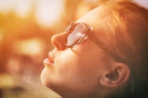 Woman in sunglasses looking up at the sun, mindful of skin cancer risks